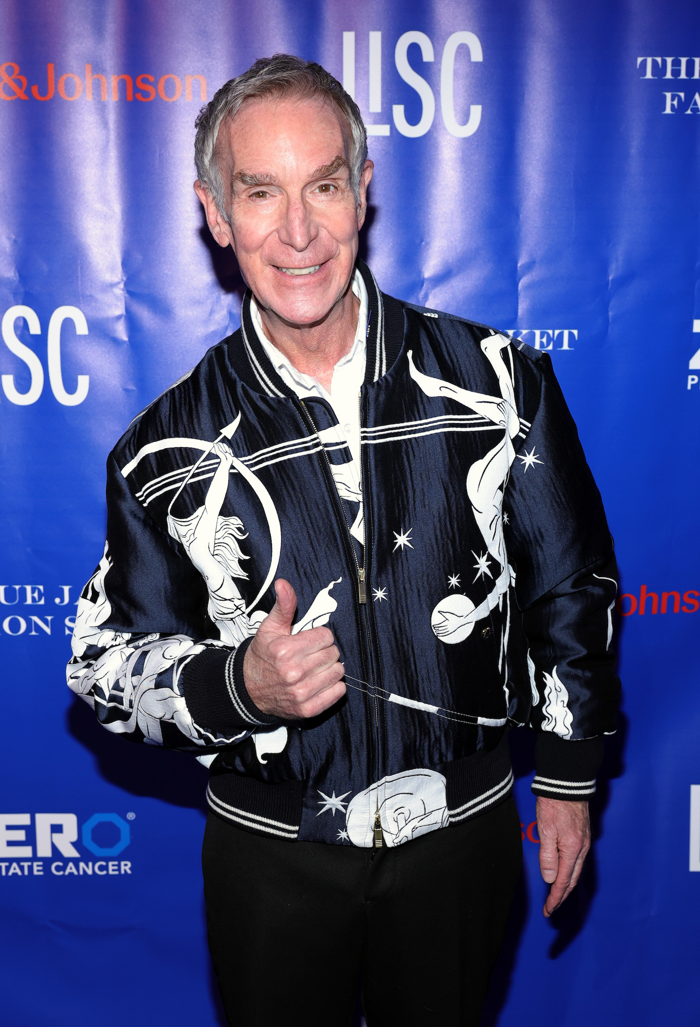 Man successful  a patterned bomber overgarment   giving a thumbs up   connected  a bluish  carpet astatine  a personage  event