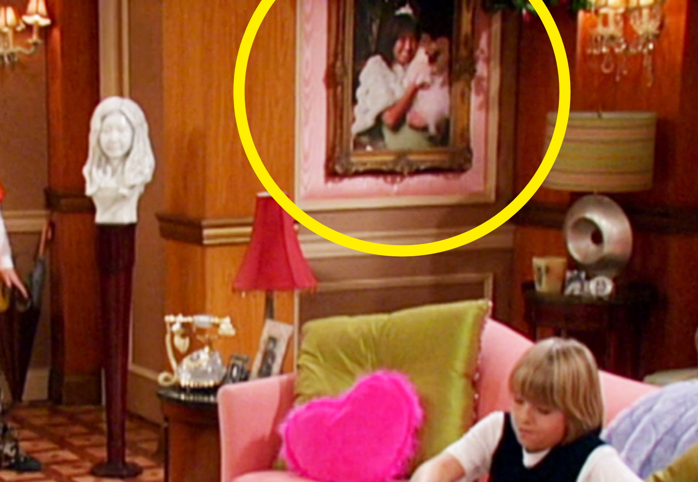 Room with classic decor, a couch, a pink heart pillow, and a framed portrait above. A child sits on the couch, engaged in an activity