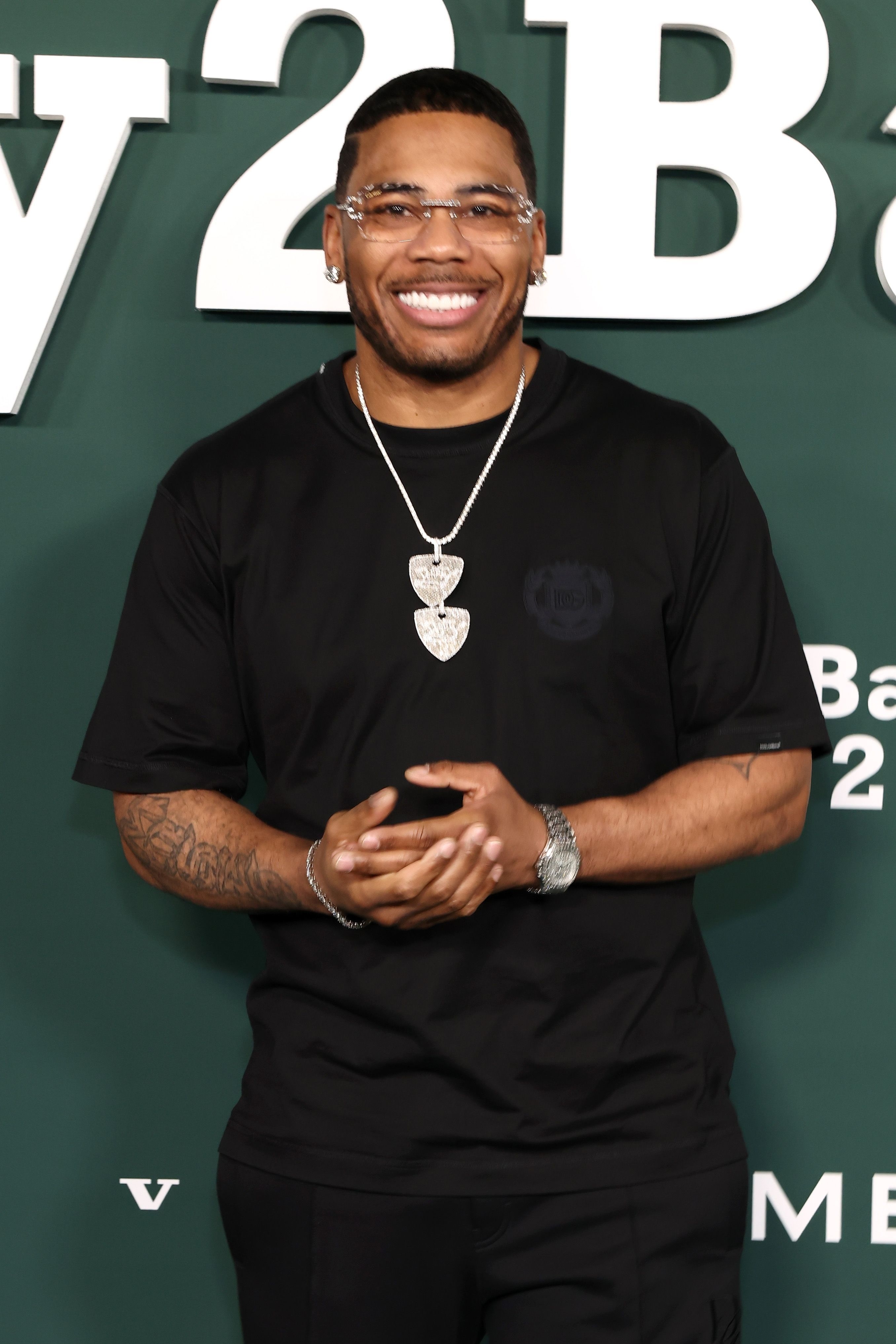 Person smiling, wearing a achromatic  T-shirt and layered concatenation  necklaces, lasting  successful  beforehand   of a step-and-repeat backdrop