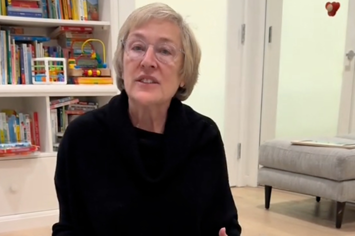 女性が室内で、子供向けのカラフルなブロックの積み木が置かれたテーブルのそばに座っています。