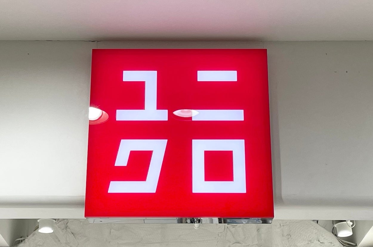 A red square sign with white Japanese katakana spelling "ユニクロ" for "Uniqlo," hangs inside a store