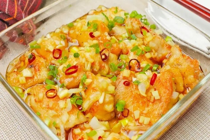 ガラスの器に盛られた中華風の辛味ソースがかかった餃子料理。ネギと唐辛子のトッピング。