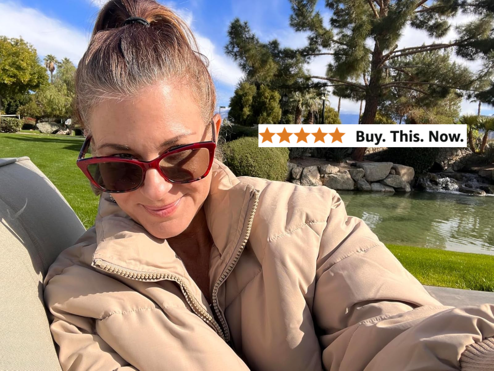 Person outdoors in a park setting, wearing sunglasses and a puffy jacket, smiling at the camera