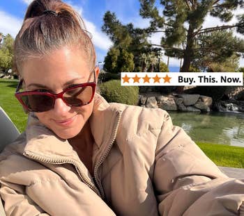 Person outdoors in a park setting, wearing sunglasses and a puffy jacket, smiling at the camera