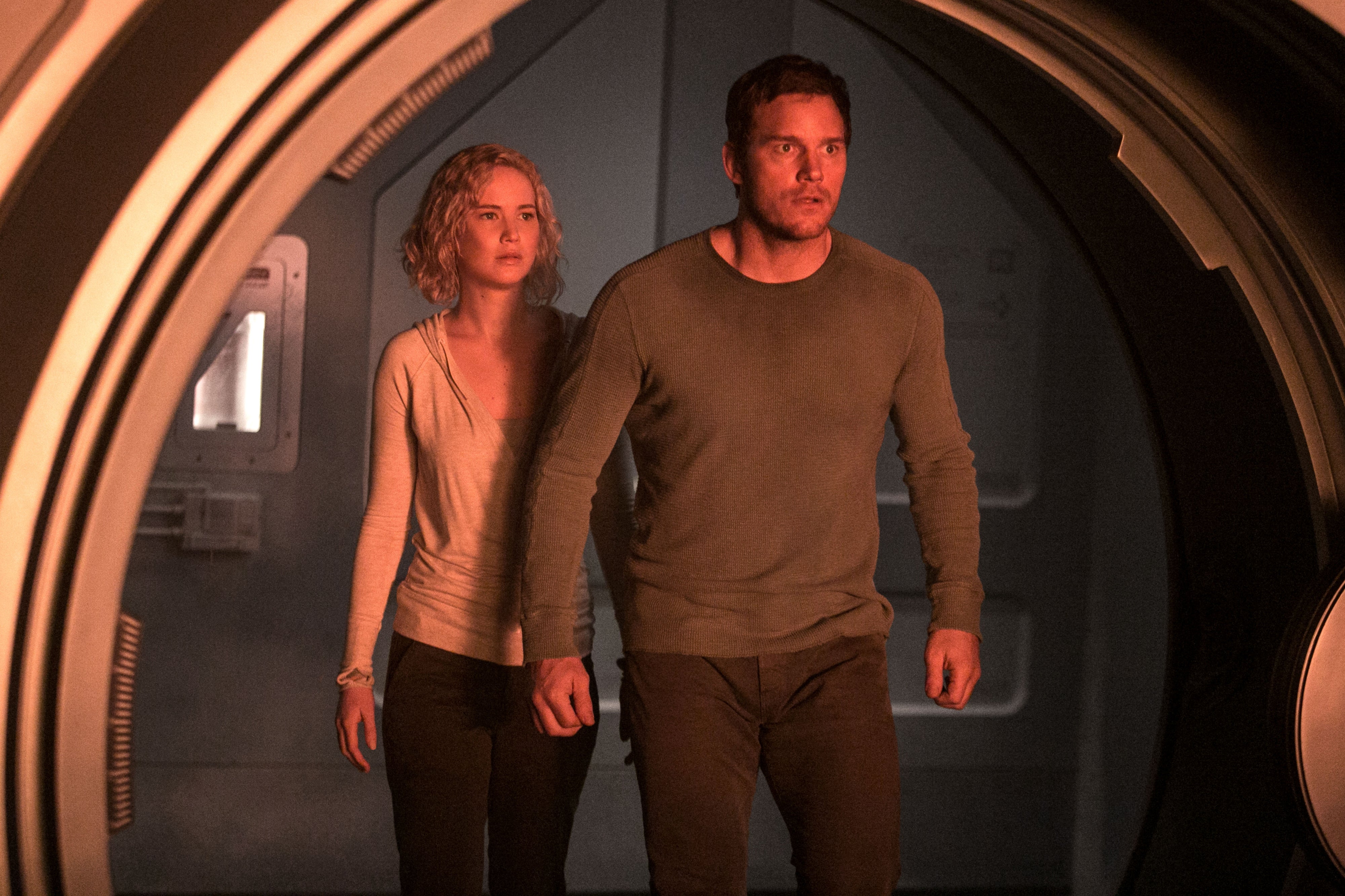 Two people in casual clothes appear inside a sci-fi setting, looking focused and cautious
