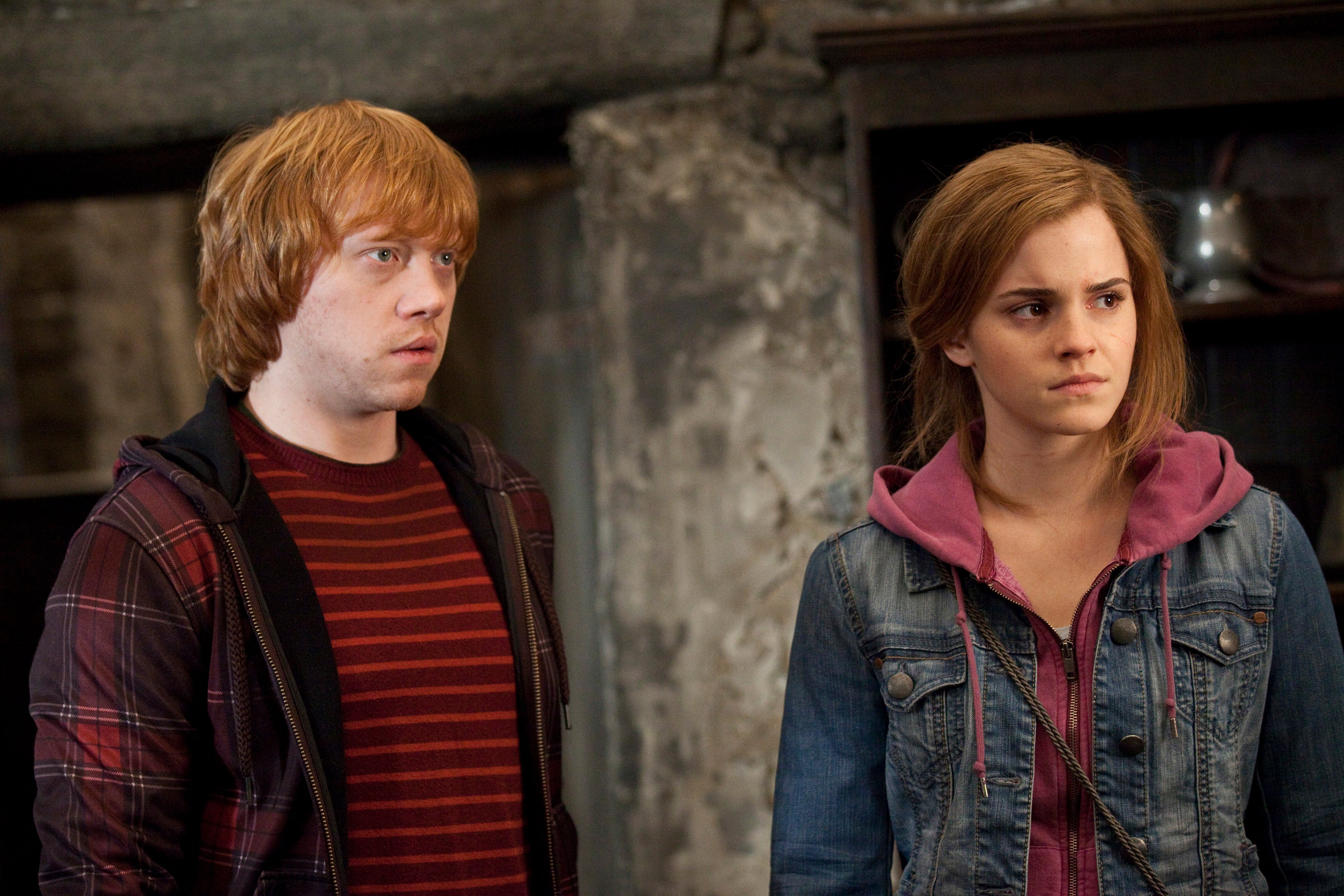 Two individuals indoors, one in a striped shirt and plaid jacket, the other in a hoodie and denim jacket, both with serious expressions