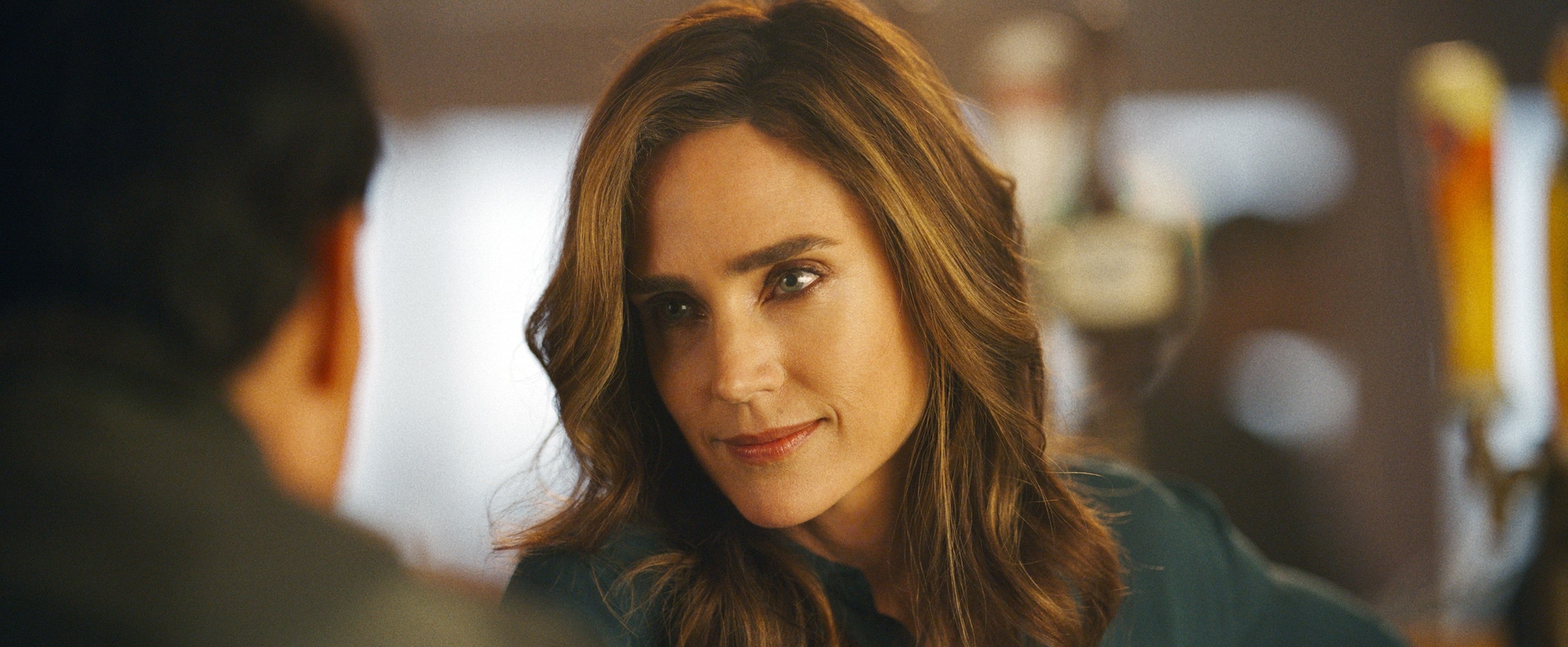 A person with long hair is engaging in conversation, looking attentively at someone off-camera. The setting appears to be indoors