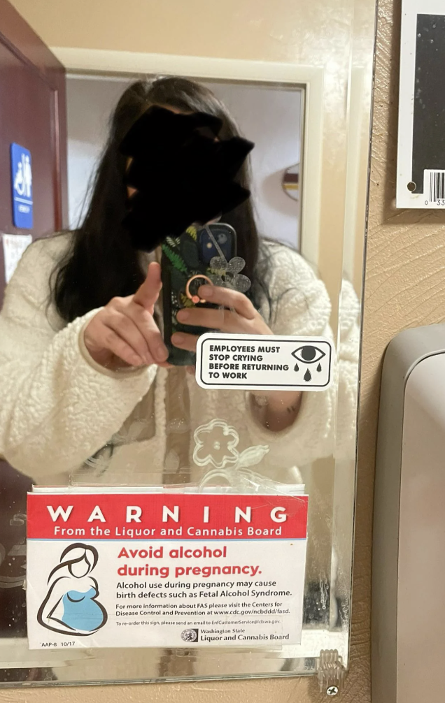 Person successful  a fluffy overgarment   taking a selfie successful  a nationalist   restroom mirror. There's a humorous sticker and a gestation  intoxicant  informing  connected  the mirror