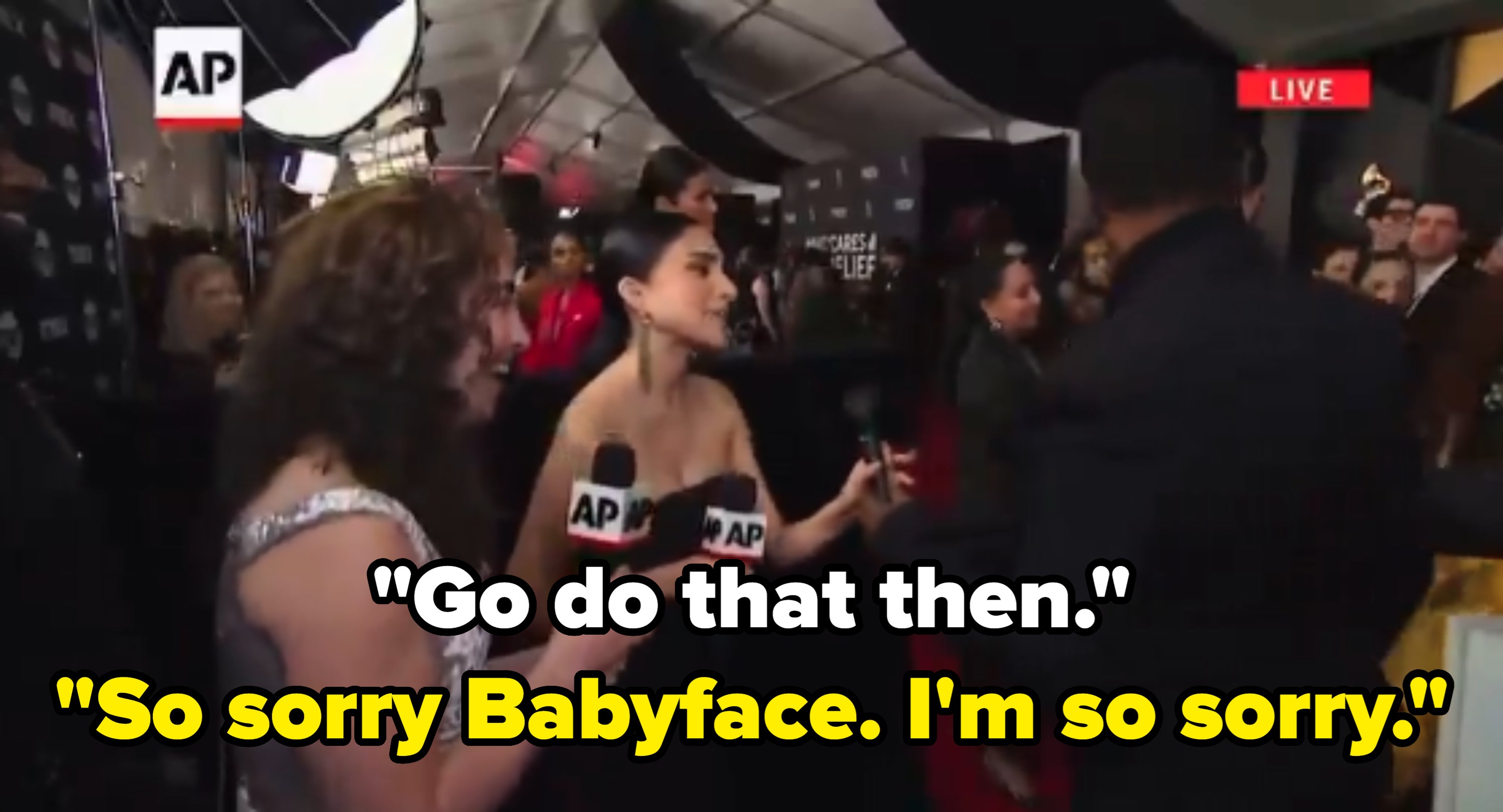 Two reporters interview a celebrity at an event. The celebrity wears a sleek black outfit amidst a busy, crowded backdrop