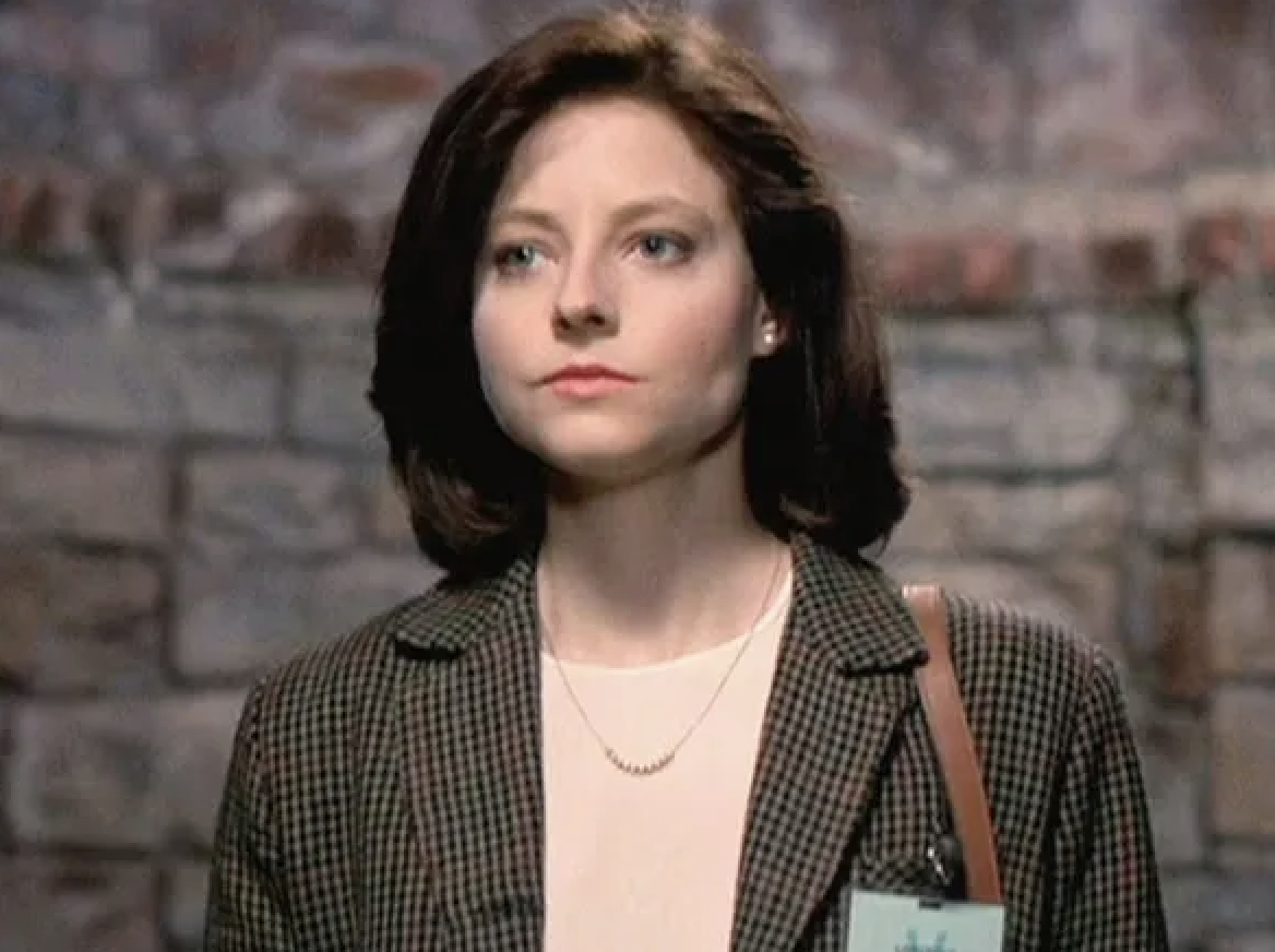 Person in a professional outfit with a blazer, standing against a stone wall background
