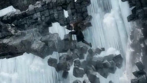 Person scaling a large, crumbling stone wall amidst cascading waterfall