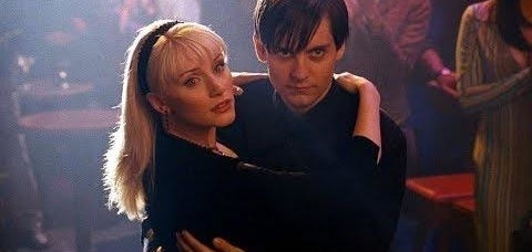 A couple dances closely in a dimly lit room, surrounded by people. They are focused, creating an intimate atmosphere