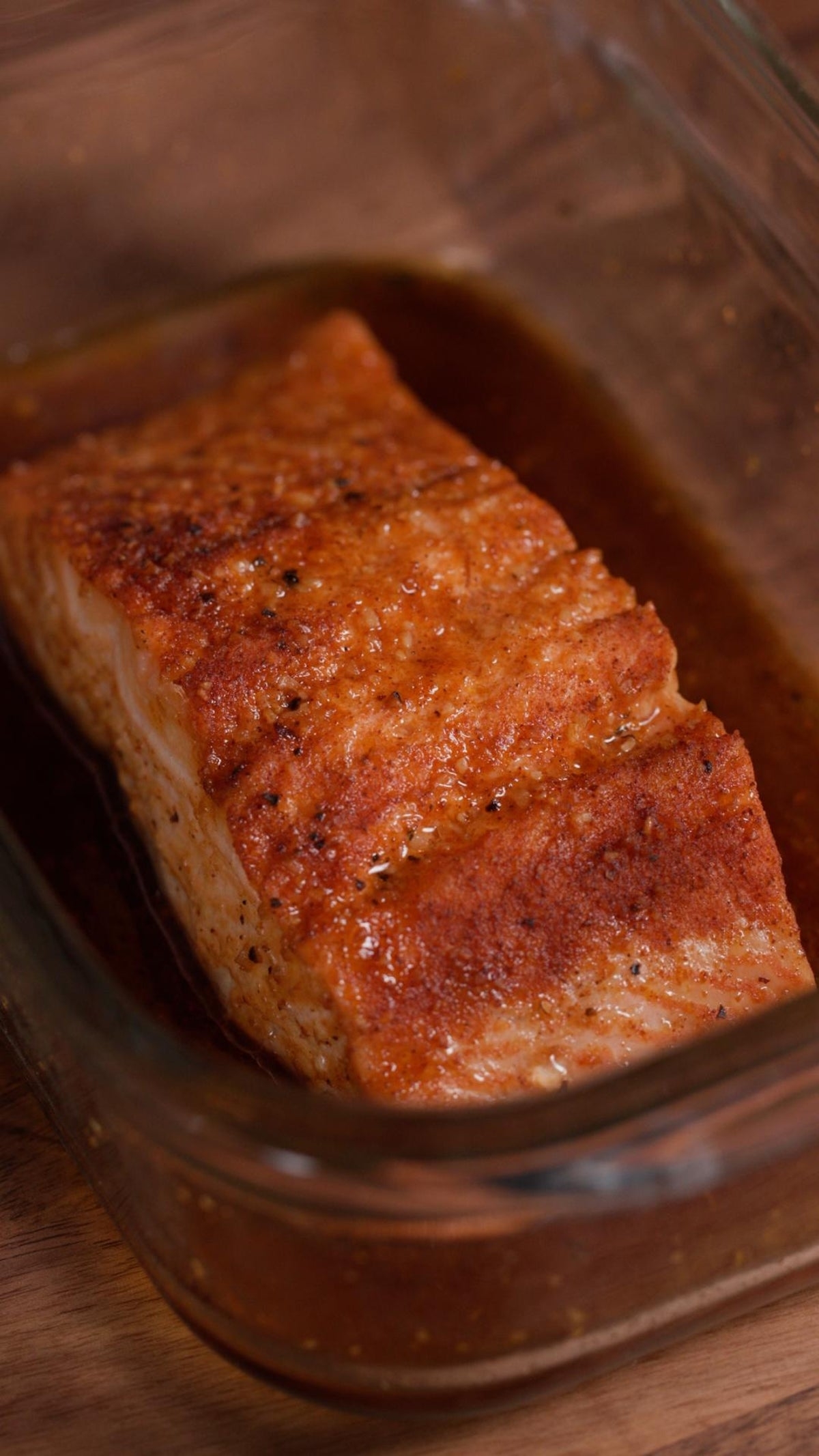 Cooked salmon fillet with crispy skin in a glass dish, seasoned with spices and broiled to perfection