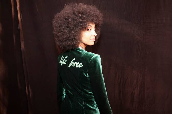 A person with curly hair wears a velvet jacket with 