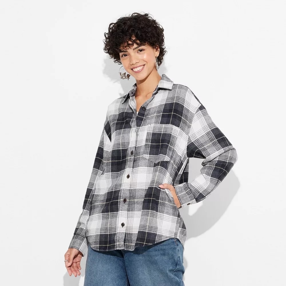 Person with curly hair wearing a plaid button-up shirt and jeans, smiling with hand in pocket, suitable for shopping fashion article