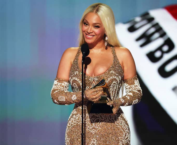 Person in an embellished gown holding a Grammy on stage, smiling