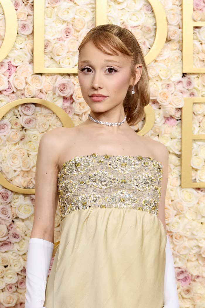 Ariana Grande in a strapless, embellished gown with a choker necklace stands in front of a floral backdrop