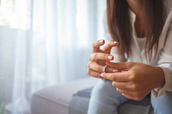 Person sitting on a couch, removing a ring from their finger, suggesting themes of relationships or breakups