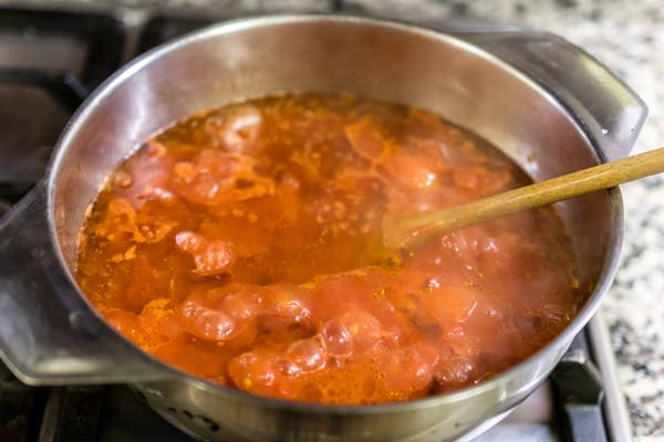 Pot of bubbling tomato sauce on a stove with a wooden spoon resting inside