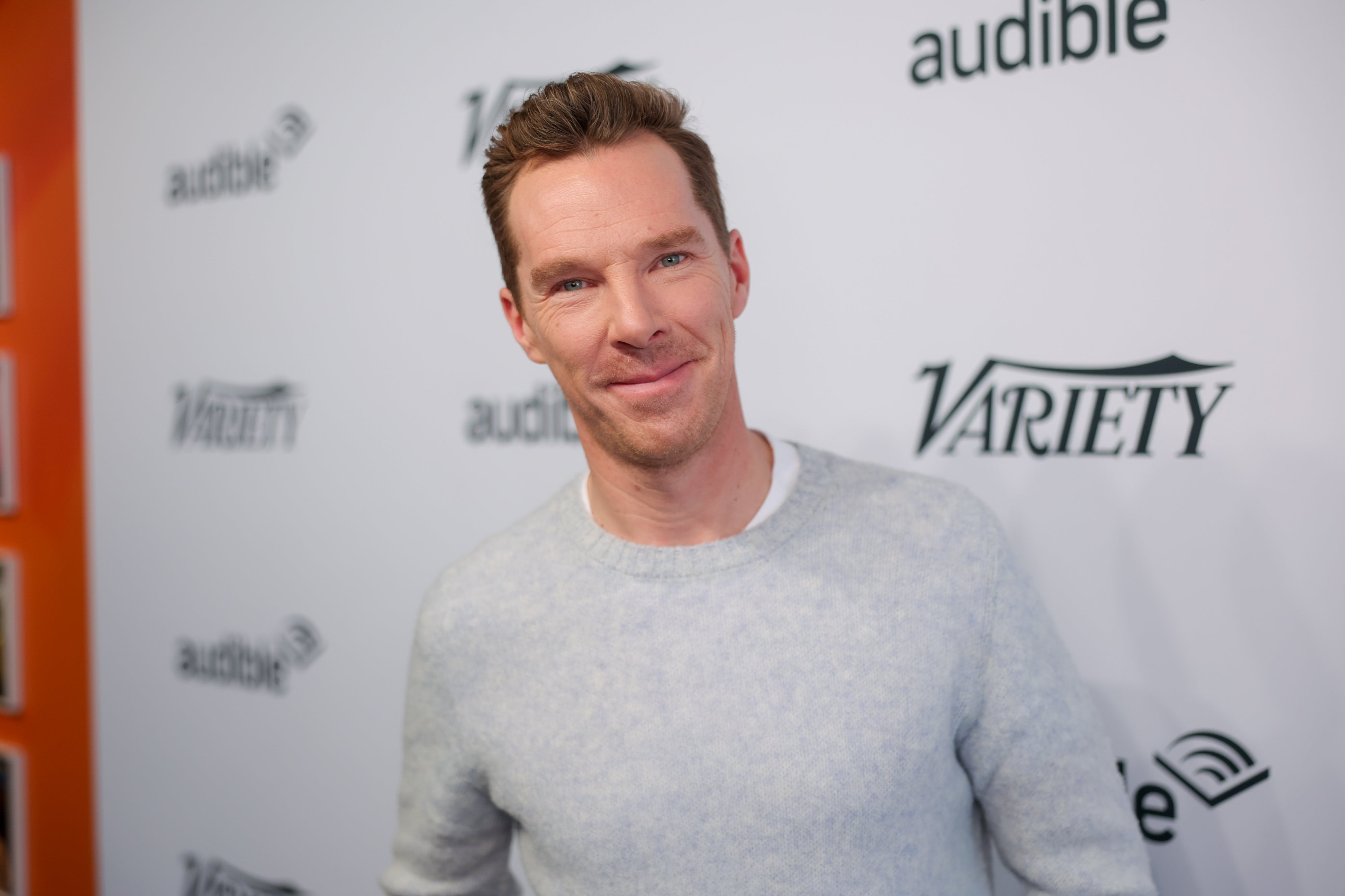 Benedict Cumberbatch in a light sweater poses at a Variety event backdrop