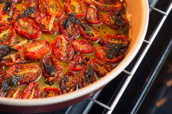 Tomato halves roasting in a pan with herbs and oil, showing some charred edges for added texture and flavor