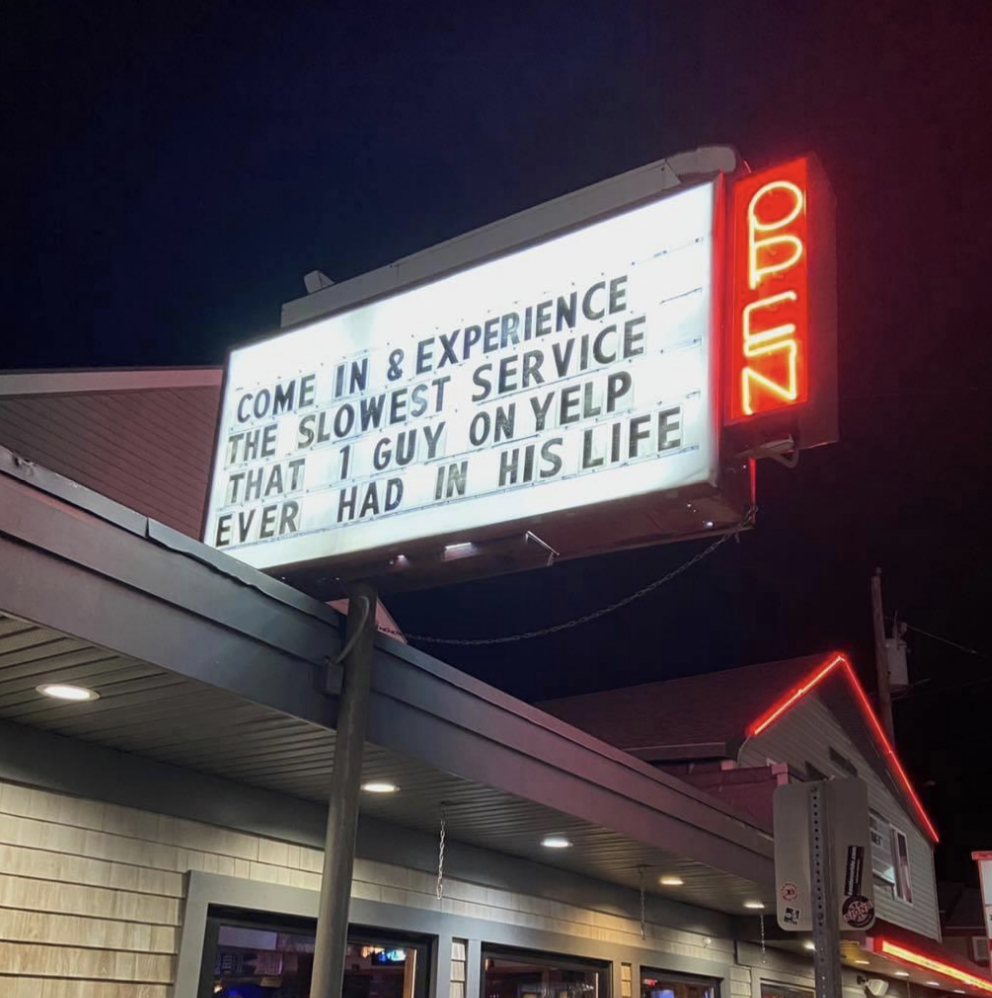 A restaurant sign humorously advertises: "Come in & experience the slowest service that 1 guy on Yelp ever had in his life," with an "open" sign