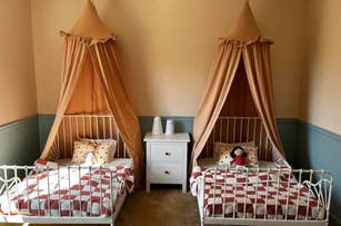Children's bedroom with two canopy beds, patterned blankets, pillows, and a nightstand with decorative items between them