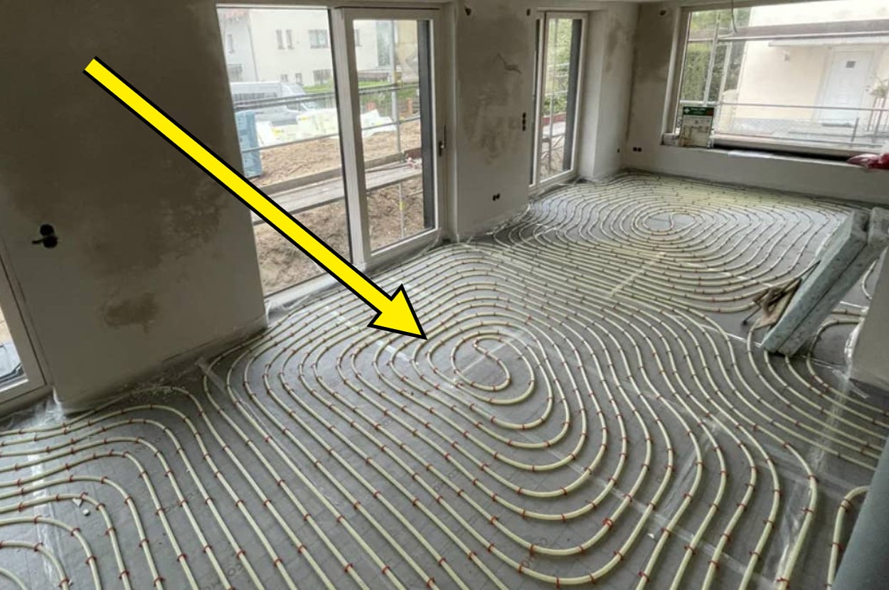 Arrow pointing to a room with neatly installed underfloor heating pipes, indicating the installation layout before flooring is added