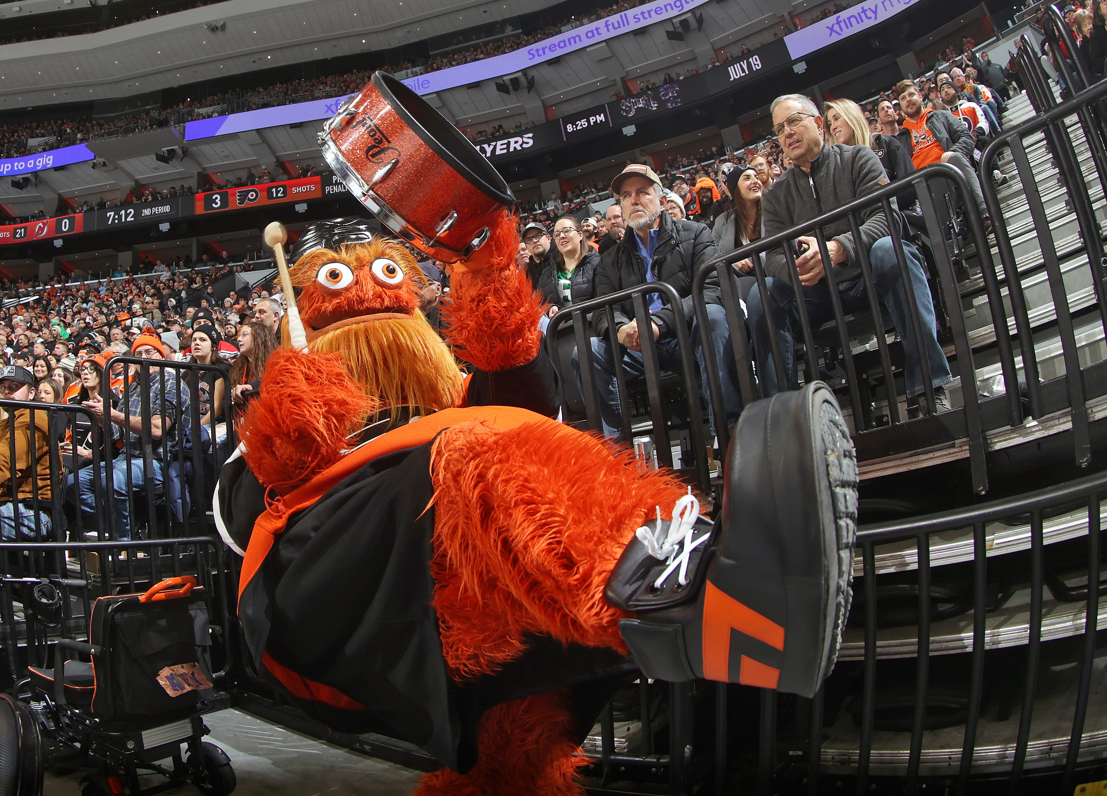 Gritty, the Mascot for the Philadelphia Flyers, bangs a drum in a crowded stadium.