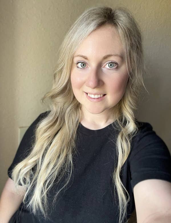 Myka with long wavy hair smiling, wearing a simple black T-shirt, standing indoors