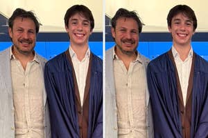 A young graduate in a gown and a striped blazer stands happily with an adult in a casual blazer and shirt, both smiling for a photo