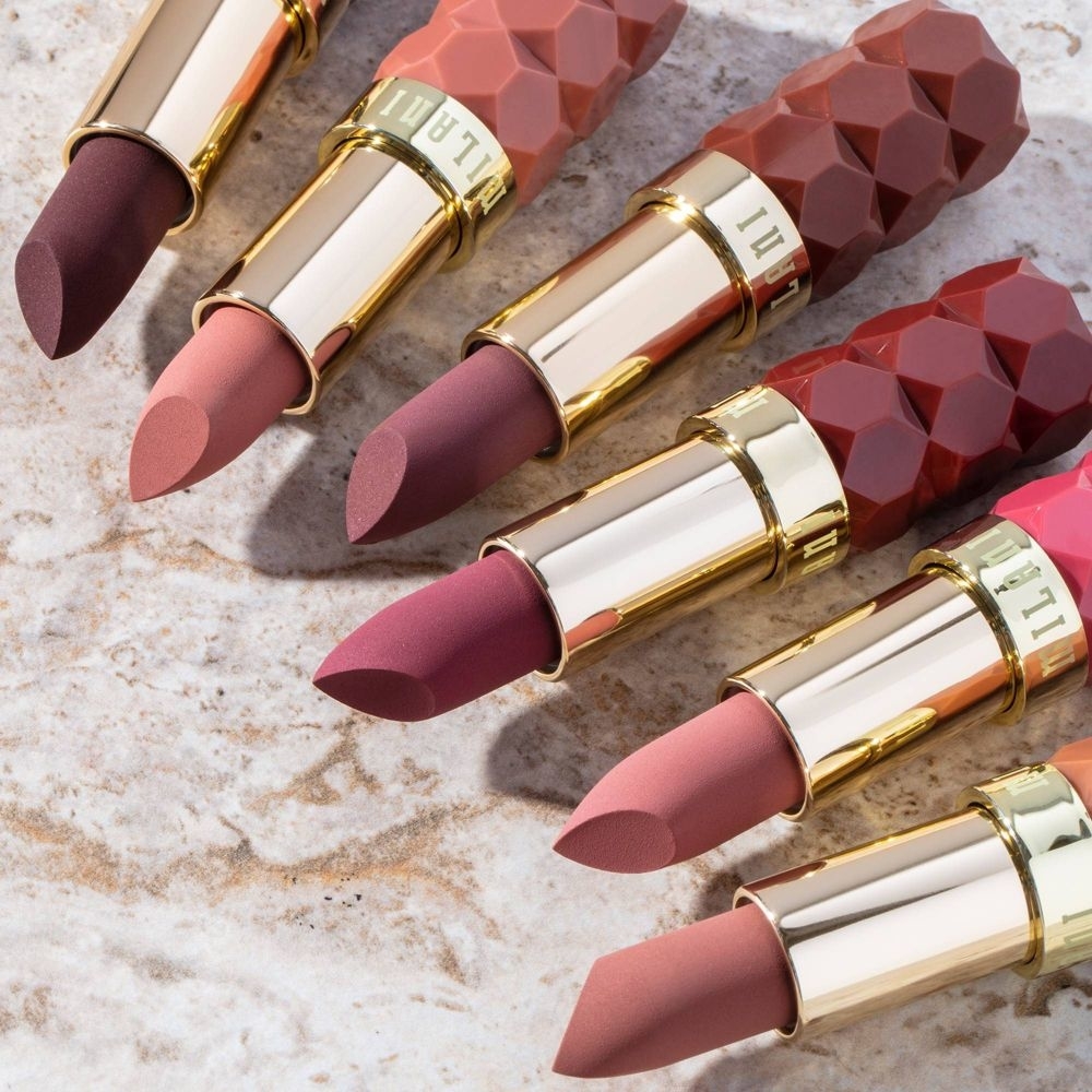 Six lipsticks with textured caps are laid out on a stone surface, showcasing varying shades of pink and brown