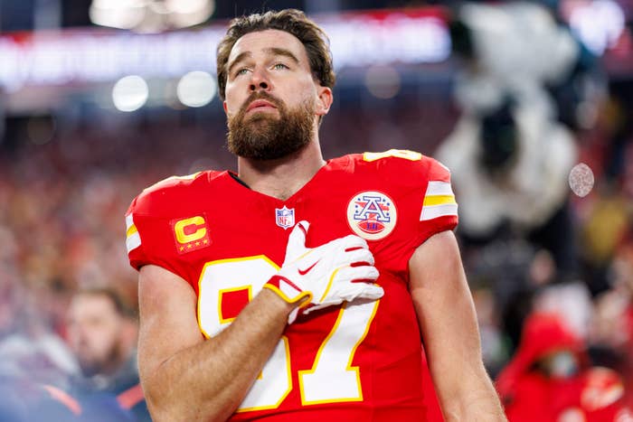 Football player stands with hand on heart during anthem, wearing a red jersey with the number 87 at a game setting