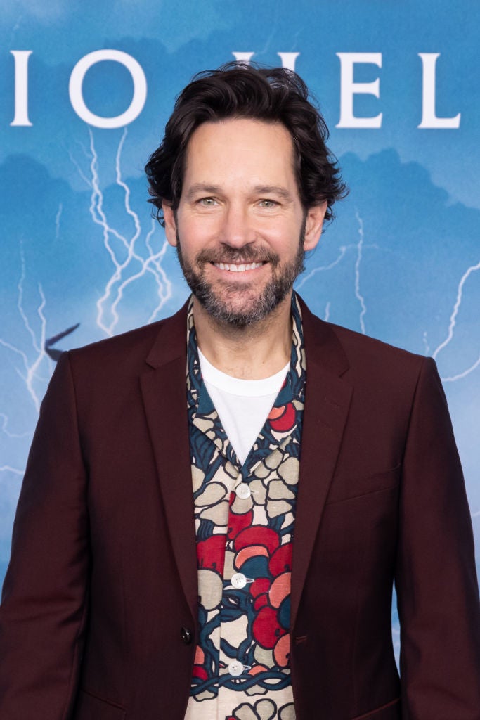 Person smiling at an event, wearing a patterned shirt under a dark jacket, in front of a backdrop with lightning design