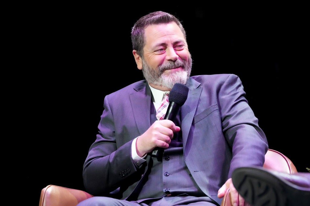 A man in a suit and tie is sitting in a chair, smiling, and holding a microphone during a speaking event