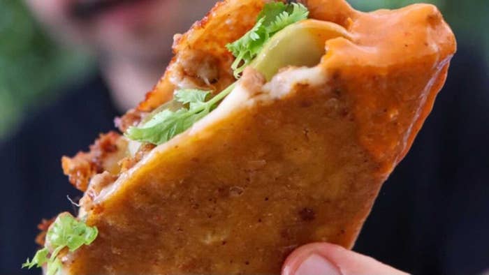 Closeup of a person holding a cheesy, crispy taco filled with cilantro and avocado