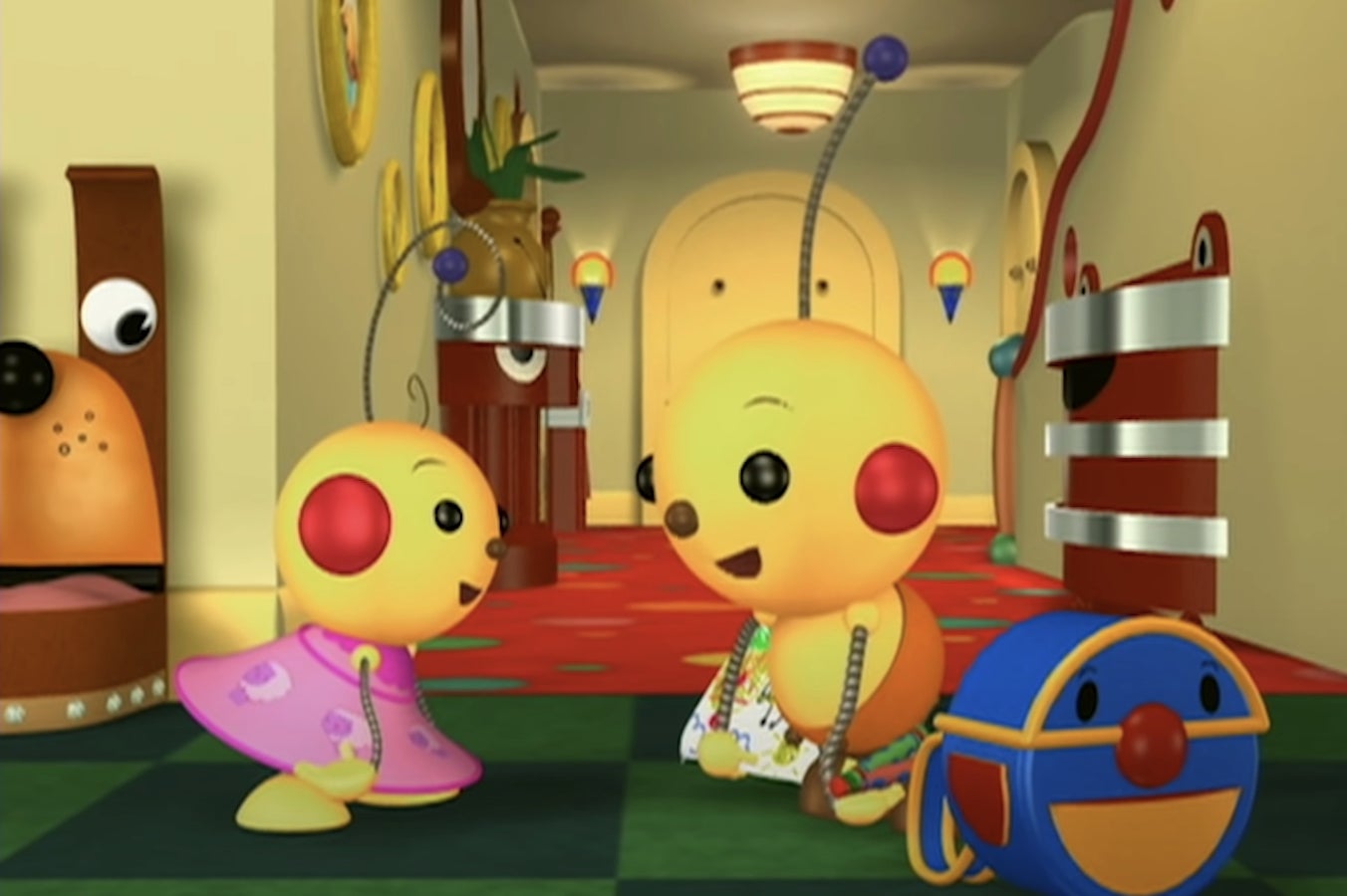 Animated robots with round bodies and antennae chat in a colorful hallway. An additional robot shaped like a ball is present