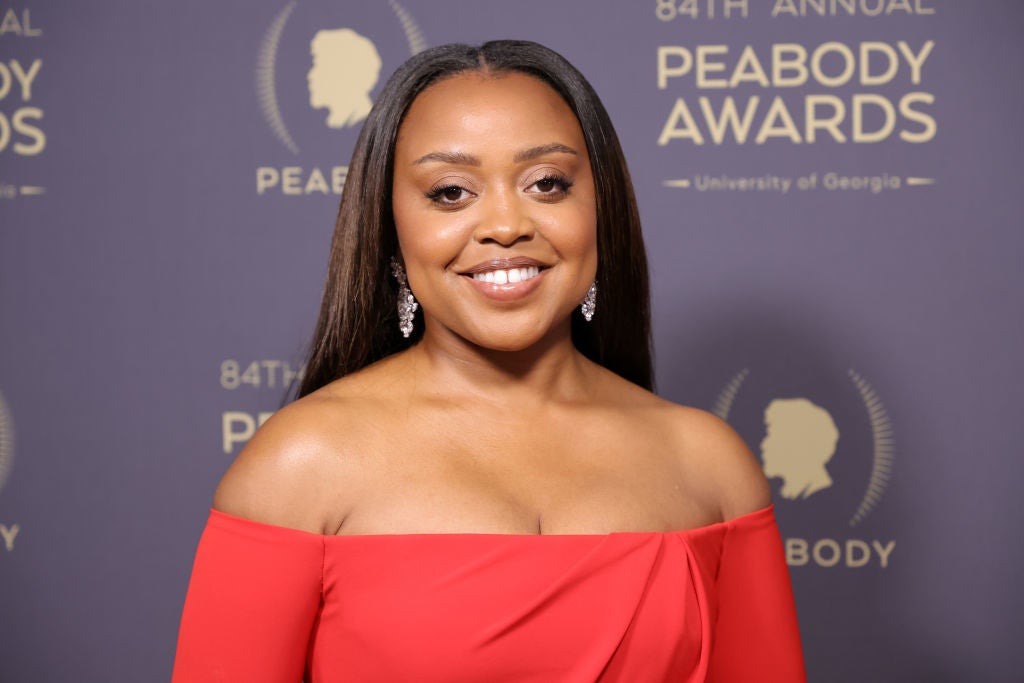 Person in elegant off-shoulder dress at the 84th Annual Peabody Awards backdrop, smiling