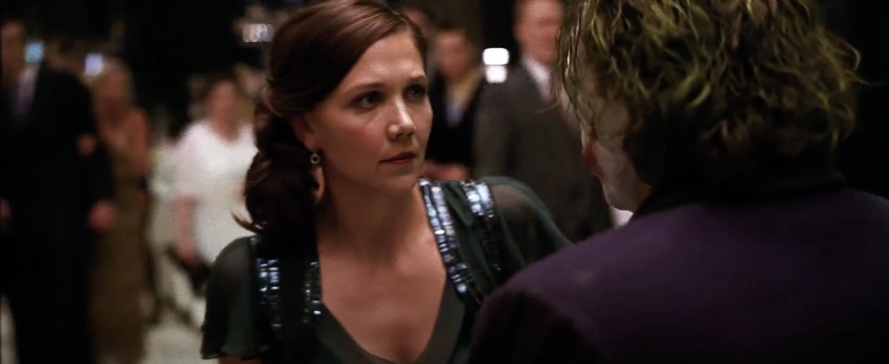 Woman in a formal dress confronts a person with unkempt hair in a crowded event setting