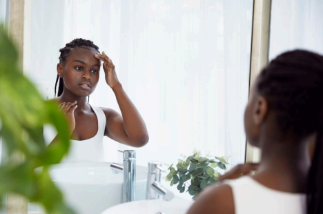 Person in front of a mirror, gently touching their face, with green plants in the foreground