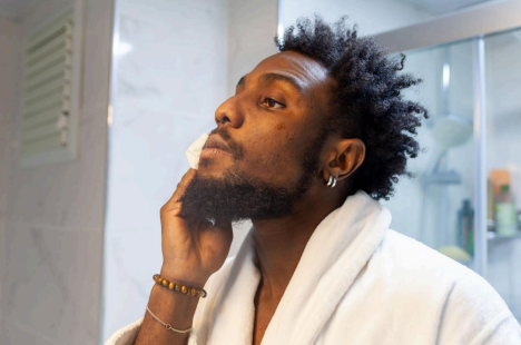 Person in a bathrobe applying skincare product on face in a bathroom setting