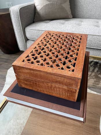 reviewer's wooden decorative box with star-shaped cutouts on a coffee table, placed on top of two stacked books in a living room setting