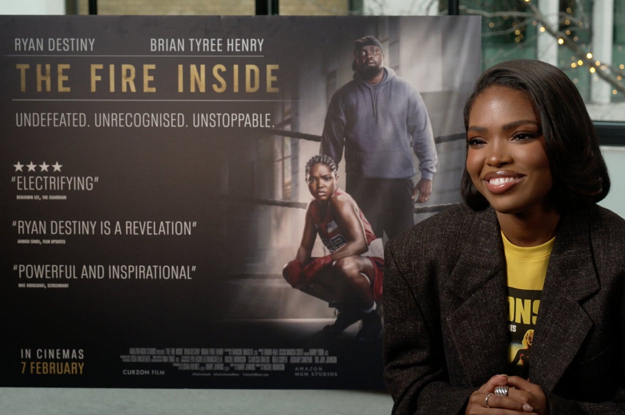 Person smiling beside a movie poster for "The Fire Inside." The poster features a boxer and quotes praising the film