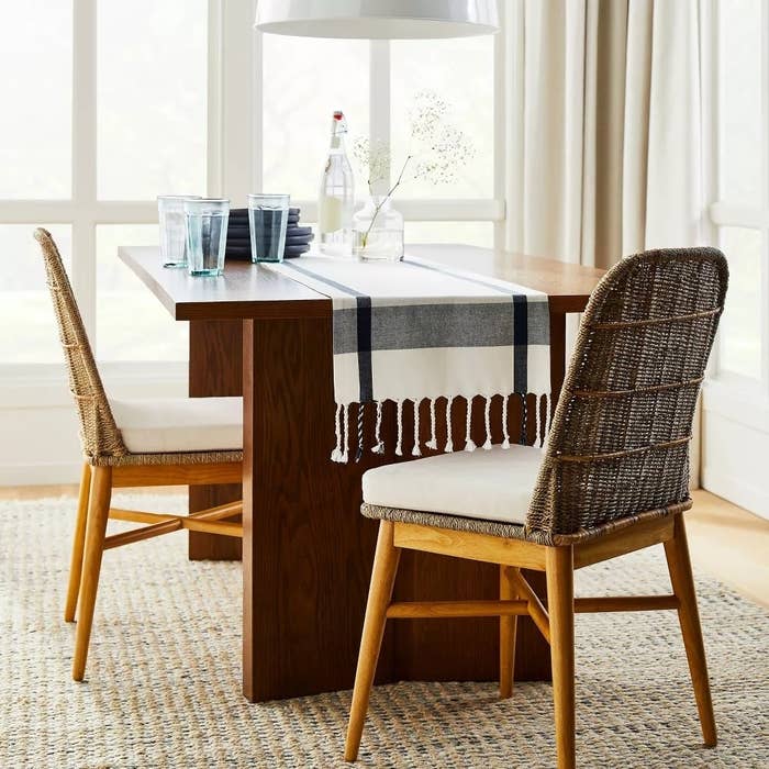 Dining array  acceptable   with wicker chairs, a runner, glassware, and a carafe arranged connected  a woven rug, successful  a agleam  country   with ample  windows
