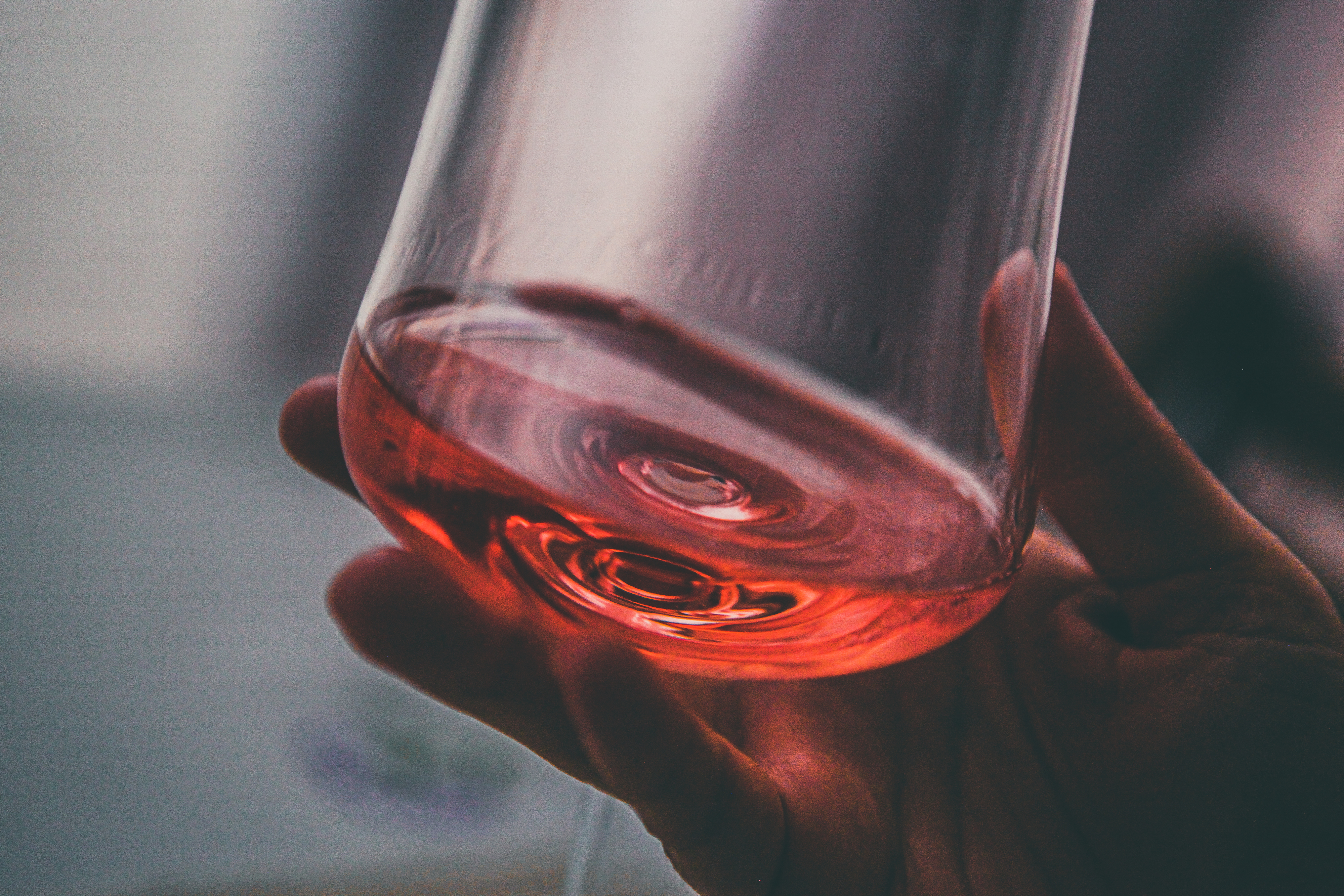Nærbilde av en hånd som holder et glass rosévin, vippet for en klar utsikt over væsken inni