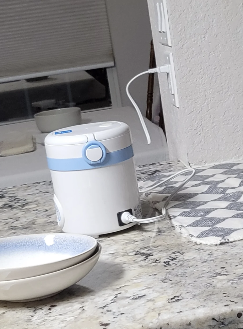 Electric appliance connected  a room  antagonistic  with a checkered mat and stacked bowls nearby. The appliance is plugged into the wall