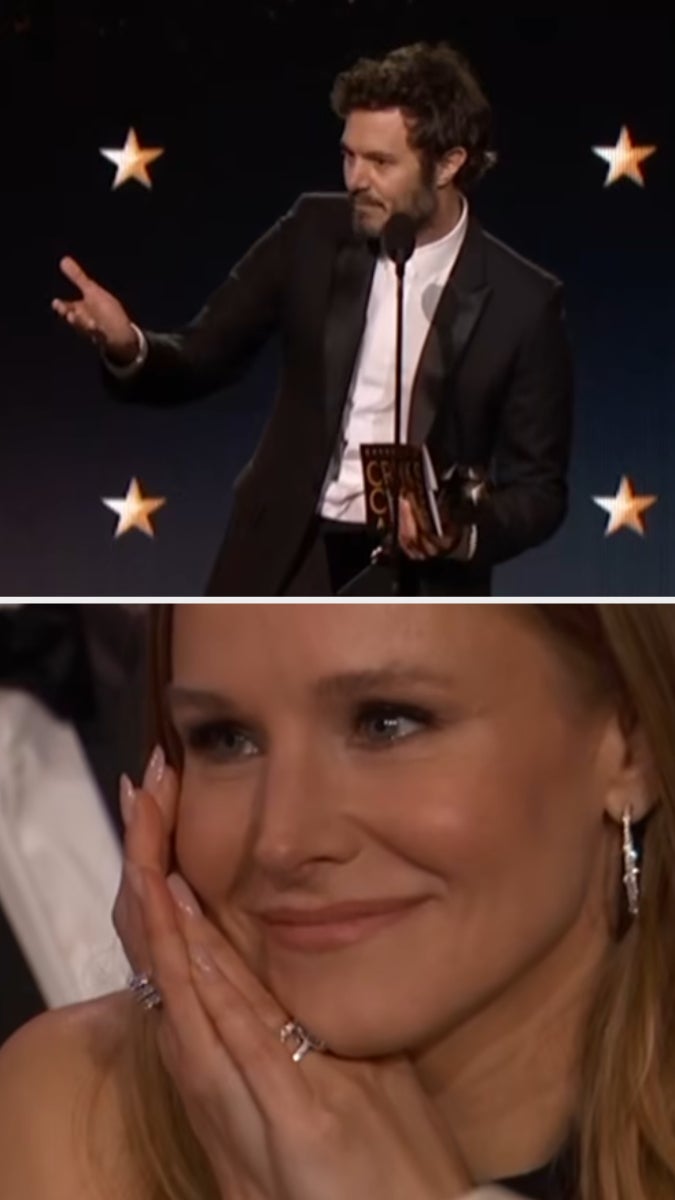 Man in suit accepts award on stage; woman in audience smiles, resting her chin on her hands