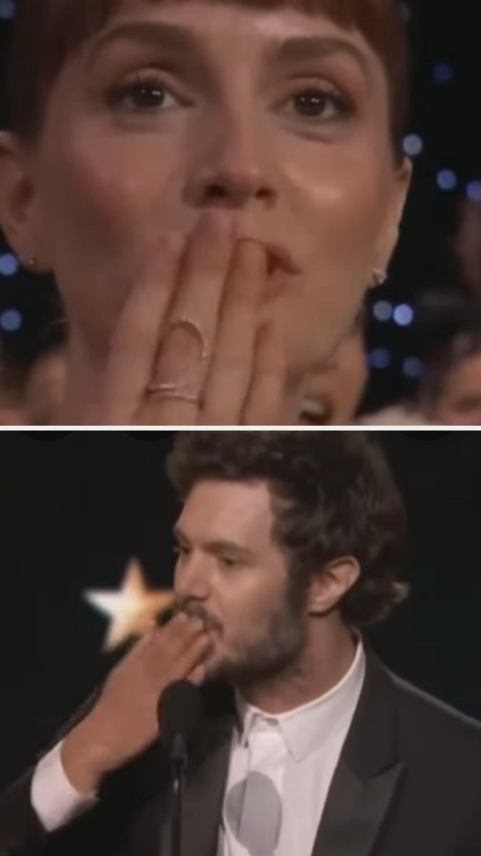 Two people at an award show, both blowing kisses. The woman has short hair and wears rings; the man wears a suit. They appear emotional