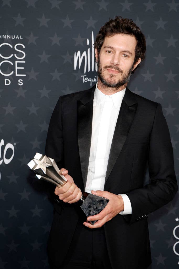Man in a black suit holding a star-shaped award poses on a red carpet at a celebrity event