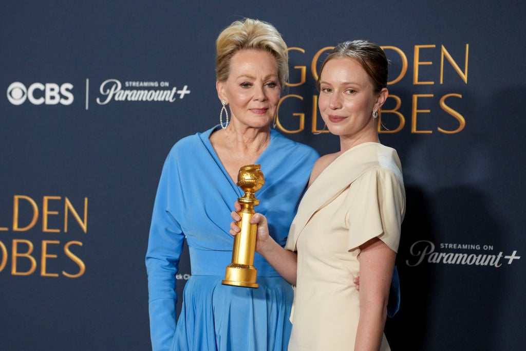 Two people on a red carpet; one is holding a Golden Globe trophy. Both are elegantly dressed in formal attire